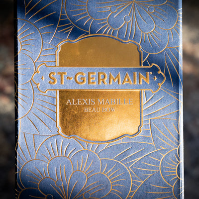 St-Germain x Alexis Mabille coffret édition limitée, comprenant une bouteille art déco, une bouteille de St-Germain, une grande pince à ingrédients dorée, une boîte renfermant des pétales d’or